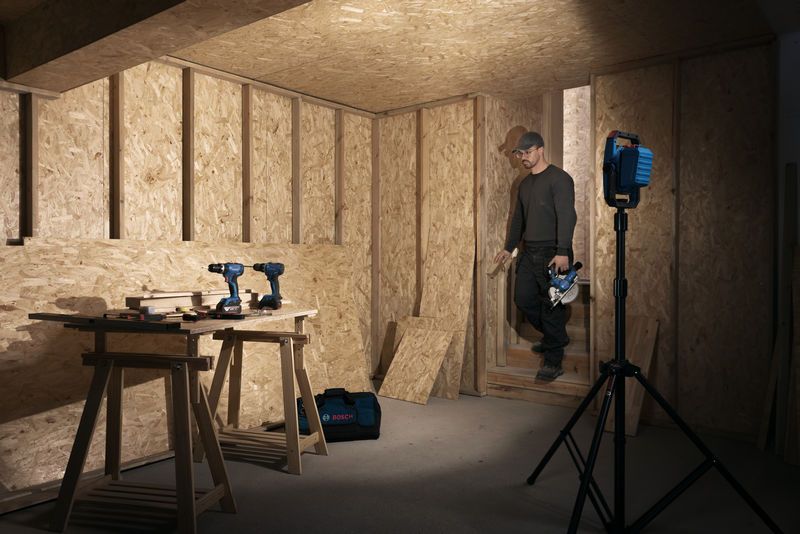 Một người mặc đồ bảo hộ đi vào xưởng gỗ được chiếu sáng bằng đèn công trường không dây.