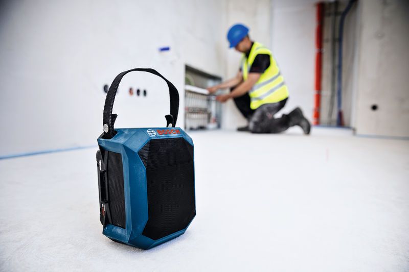 Loa Bluetooth trên sàn công trường xây dựng, phía sau có người mặc đồ bảo hộ.