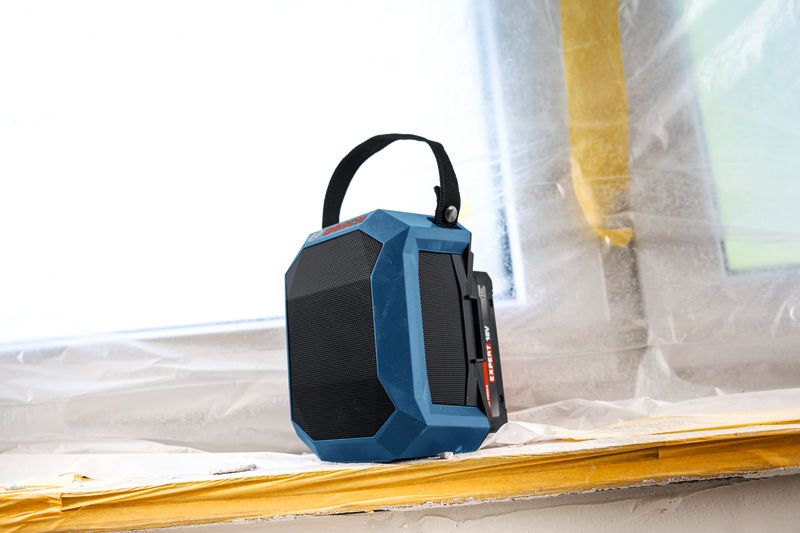 Loa Bluetooth màu xanh có tay cầm được đặt trên bệ cửa sổ tại một công trường xây dựng.