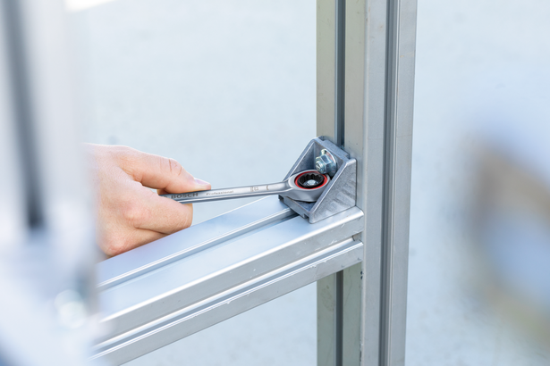 Người này dùng cờ lê bánh cóc để siết chặt một bu lông trên mối nối khung kim loại.