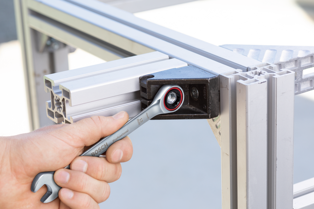 Một người đang siết chặt một con bu lông trên khung kim loại bằng cờ lê có tay quay.