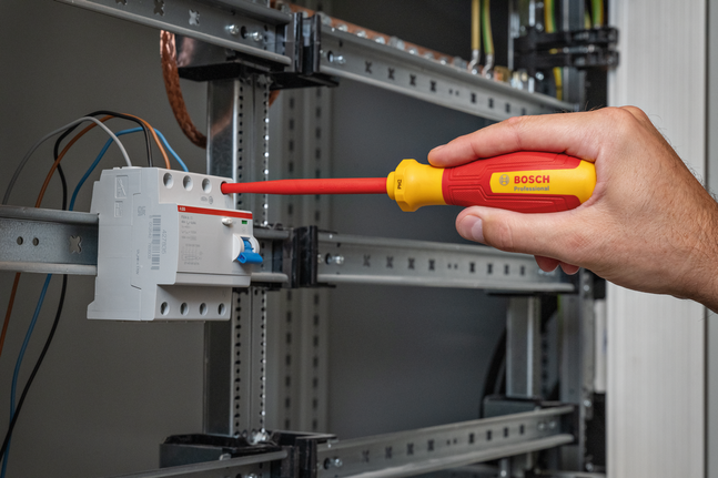 Một người đang siết chặt một con ốc trên bảng điện bằng tua vít cách điện.