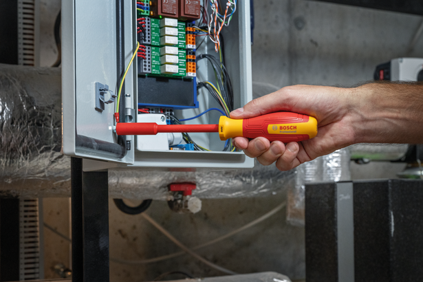 Một người đang dùng tua vít cách điện để điều chỉnh dây điện bên trong bảng điều khiển điện.