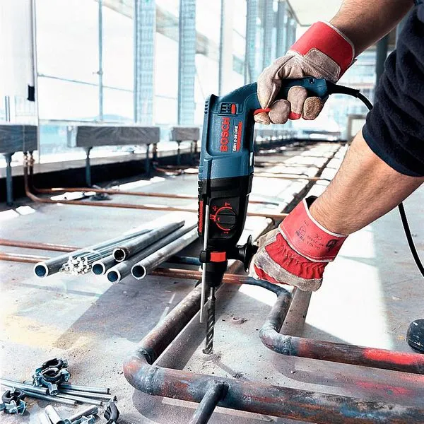 GBH 2-26 DRE Một người mặc đồ bảo hộ đang khoan vào ống kim loại tại công trường xây dựng.