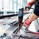 Một người mặc đồ bảo hộ đang khoan vào ống kim loại tại công trường xây dựng.