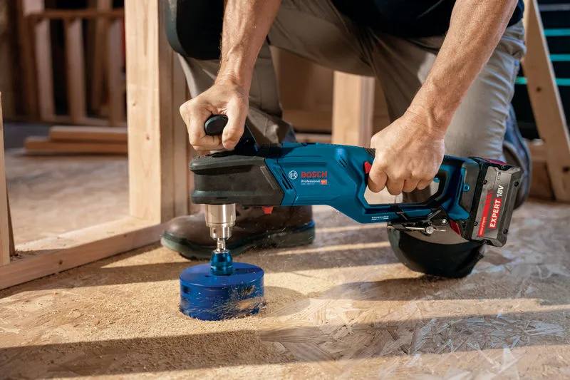 Một người sử dụng máy khoan góc không dây để khoan một lỗ lớn trên sàn gỗ.