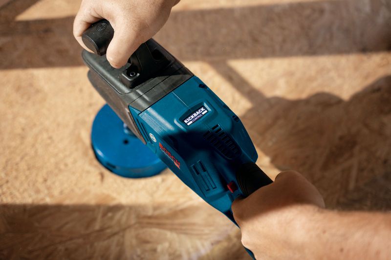 Một người đang sử dụng máy khoan góc không dây màu xanh trên bề mặt gỗ.