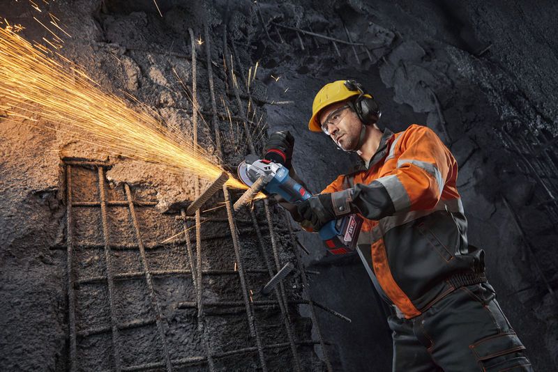 Một người đàn ông mặc đồ bảo hộ đang dùng máy mài góc để cắt thép thanh, tạo ra tia lửa.