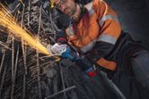 Một công nhân mặc đồ bảo hộ đang sử dụng máy mài góc để cắt thanh thép gia cường.