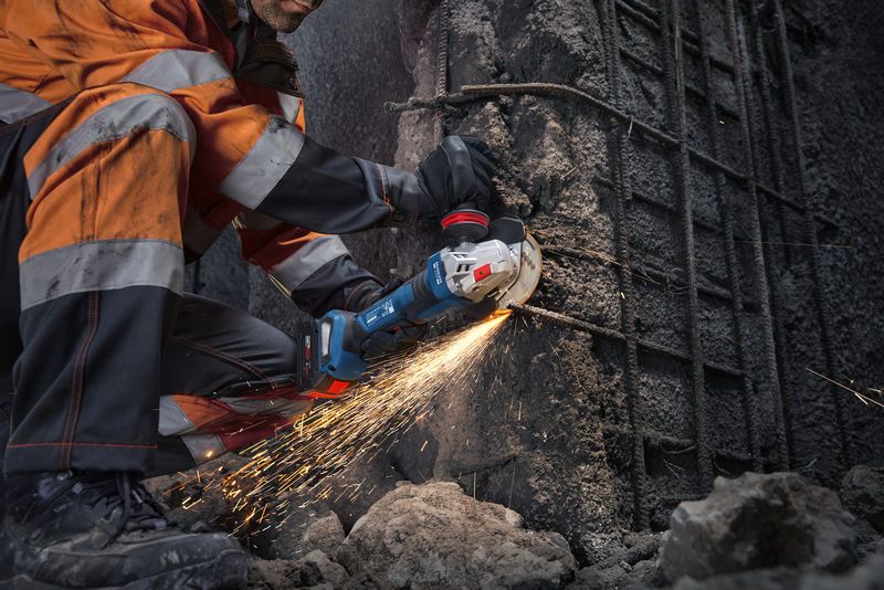 Một người đàn ông mặc đồ bảo hộ đang dùng máy mài góc cắt bê tông, tạo ra tia lửa.