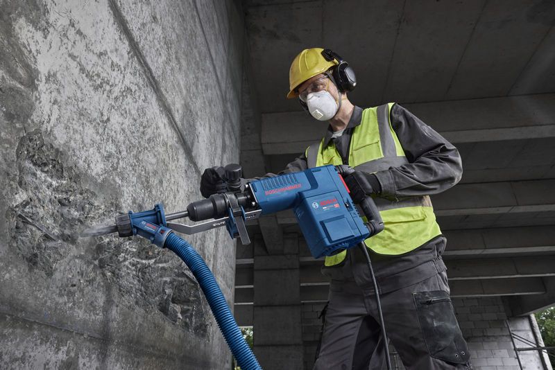 Một người đàn ông mặc đồ bảo hộ đang dùng búa phá dỡ để phá vỡ bê tông.