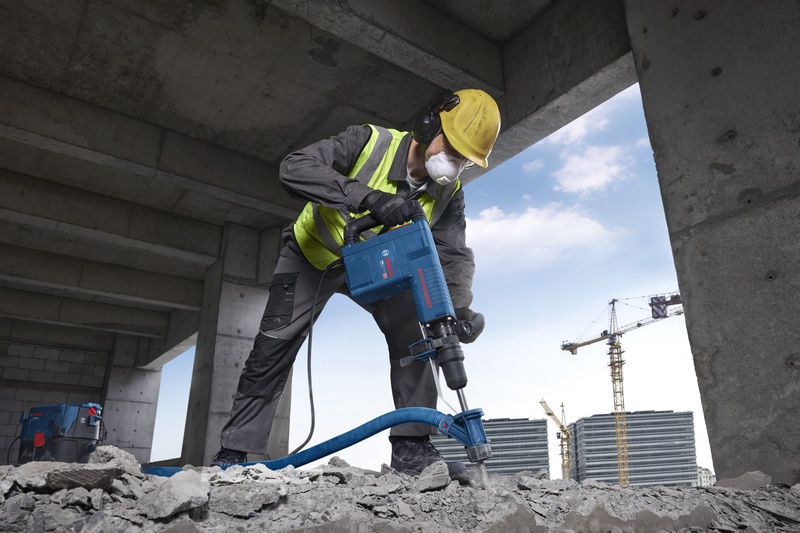 Một người đàn ông mặc đồ bảo hộ đang dùng búa phá dỡ để phá vỡ bê tông.