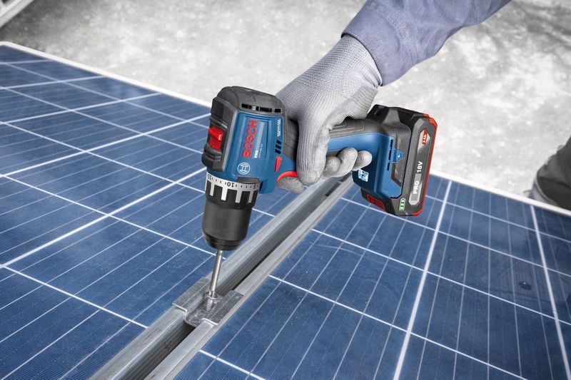 Một người mặc đồ bảo hộ sử dụng máy khoan không dây để vặn vít vào khung tấm pin mặt trời.