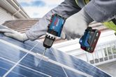 Một người đàn ông mặc đồ bảo hộ đang sử dụng máy khoan không dây trên tấm pin mặt trời.
