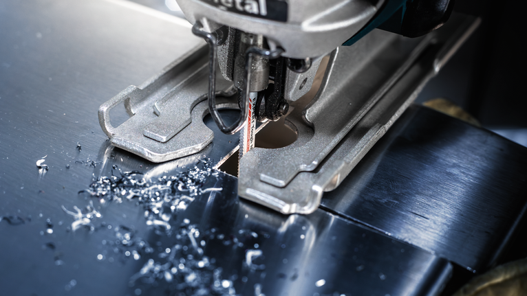 Lưỡi cưa lọng EXPERT Tough Metal thin T118AHM, 3 chiếc Máy cưa lọng cắt một tấm kim loại, các mảnh kim loại nhỏ rải rác xung quanh lưỡi cưa.