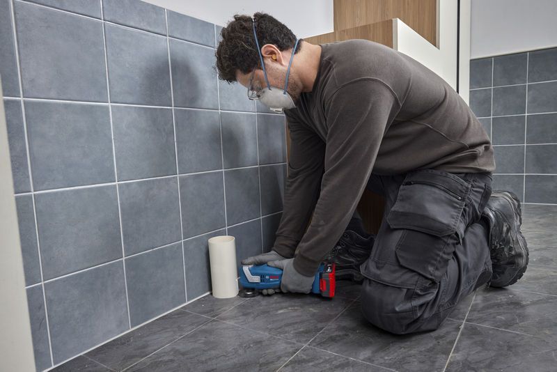 Một người mặc đồ bảo hộ đang sử dụng một công cụ đa năng để cắt gạch lát sàn.