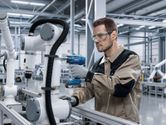 Công nhân mặc đồ bảo hộ sử dụng máy khoan không dây trên cánh tay robot công nghiệp.