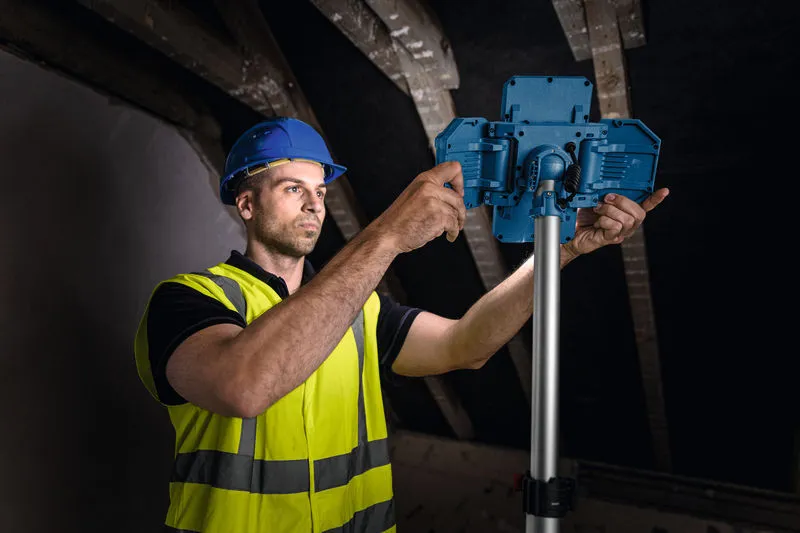 Một công nhân mặc đồ bảo hộ đang điều chỉnh đèn công trường không dây trên giá đỡ.