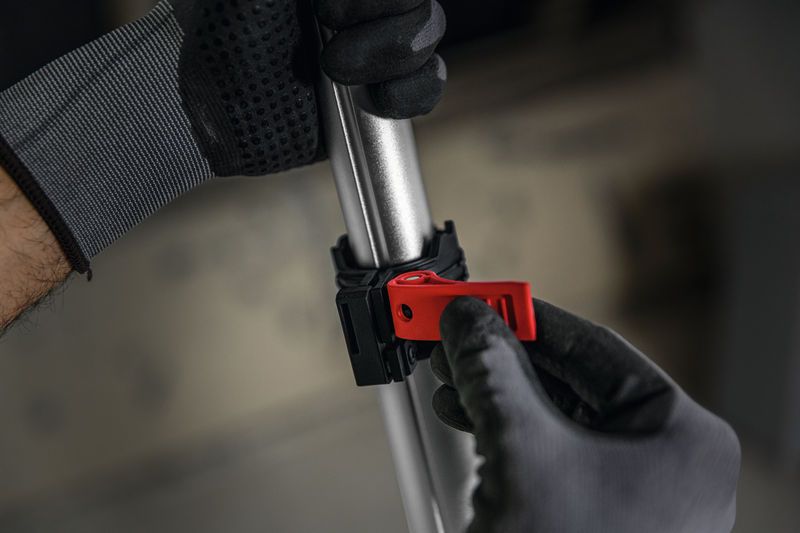 Một người mặc thiết bị an toàn đang điều chỉnh kẹp màu đỏ trên một cột kim loại.