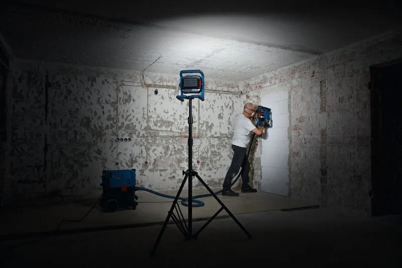 Một người mặc đồ bảo hộ đang vận hành máy khoan tường dưới ánh đèn làm việc.