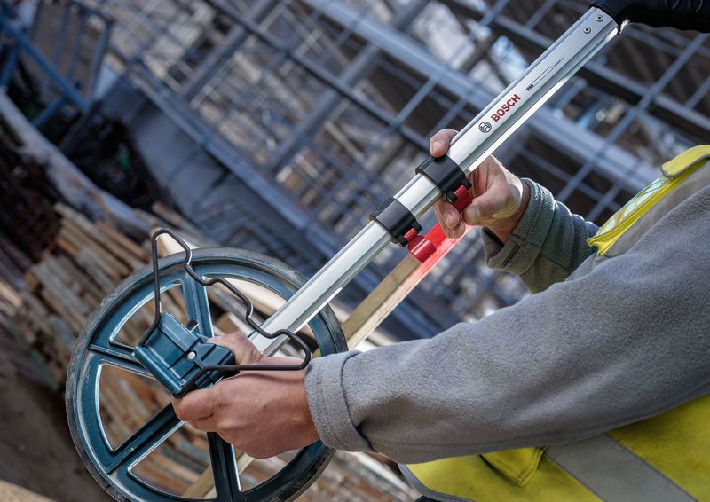 Một người đeo thiết bị an toàn đo khoảng cách bằng một bánh xe đo lớn.