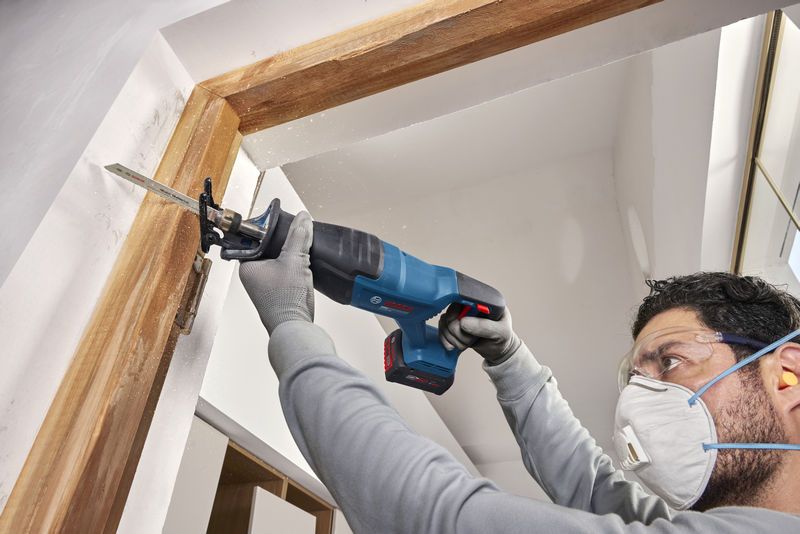 Một người mặc đồ bảo hộ đang sử dụng máy cưa lọng không dây để cắt khung cửa.