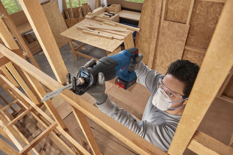 Một người mặc đồ bảo hộ đang sử dụng máy cưa lọng không dây để cắt gỗ.