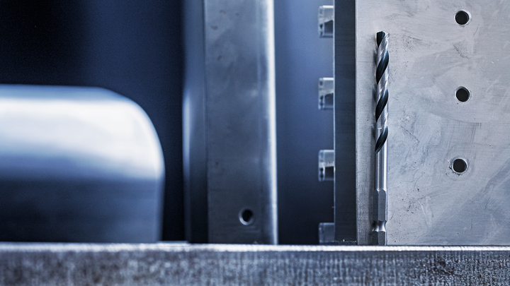 Mũi khoan kim loại được căn chỉnh theo chiều dọc bên cạnh bề mặt kim loại đã gia công có lỗ khoan.