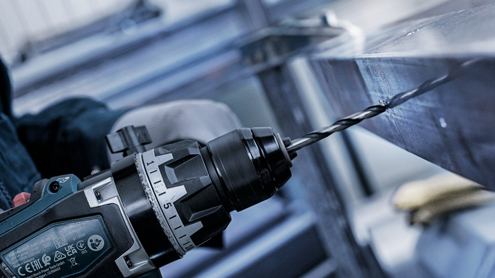 Người mặc đồ bảo hộ khoan lỗ trên thanh kim loại.