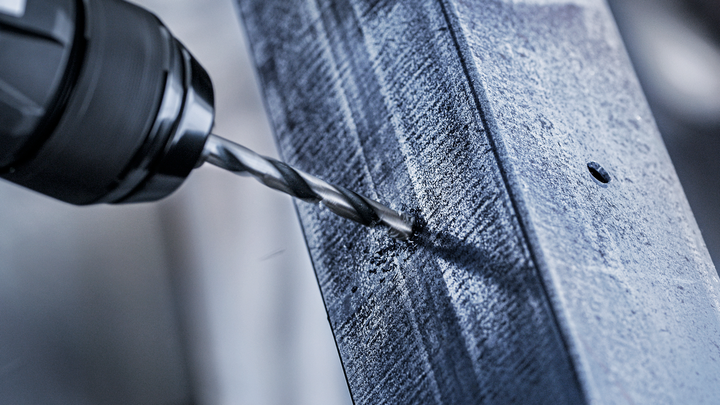 Máy khoan điện tạo ra một lỗ trên thanh kim loại.