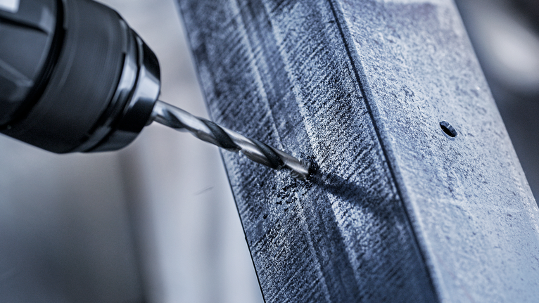 Máy khoan điện tạo ra một lỗ trên thanh kim loại.