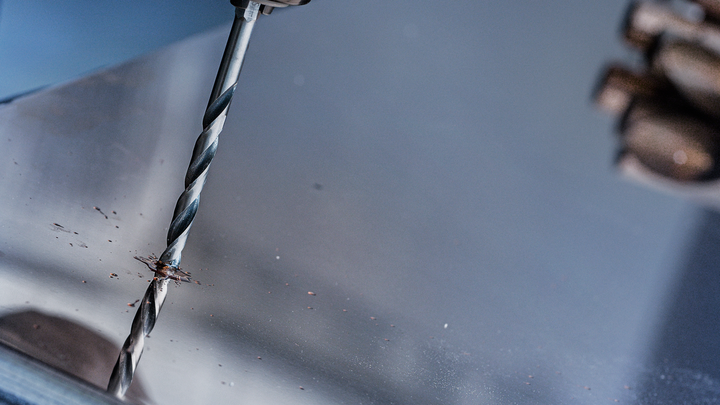 Người đang khoan vào tấm kim loại, đang đeo thiết bị an toàn.