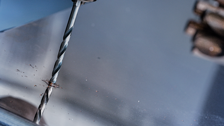 Người đang khoan vào tấm kim loại, đang đeo thiết bị an toàn.