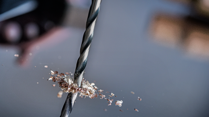 Mũi khoan tạo lỗ trên kim loại với các mảnh vụn rải rác xung quanh.