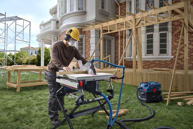 Một người đàn ông mặc đồ bảo hộ đang dùng cưa bàn cắt gỗ tại một công trường xây nhà.