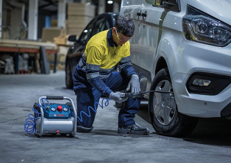 Một người mặc đồ bảo hộ đang bơm lốp xe tải bằng máy nén khí di động.