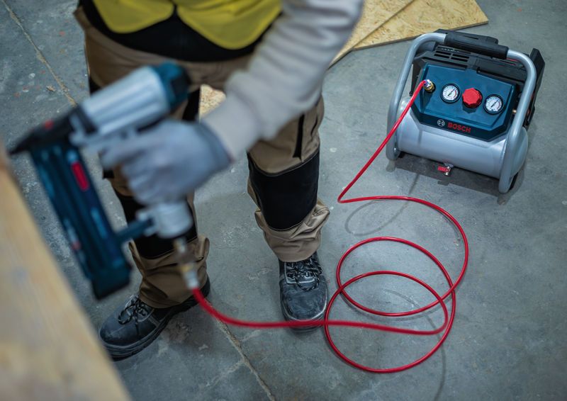 Một người mặc đồ bảo hộ đang sử dụng súng bắn đinh khí nén được nối với máy nén khí.