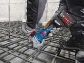 Một người đàn ông mặc đồ bảo hộ đang sử dụng máy cắt thép không dây trên lưới thép.