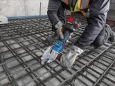 Một người đàn ông mặc đồ bảo hộ đang sử dụng dụng cụ không dây để cắt thép cây tại công trường xây dựng.