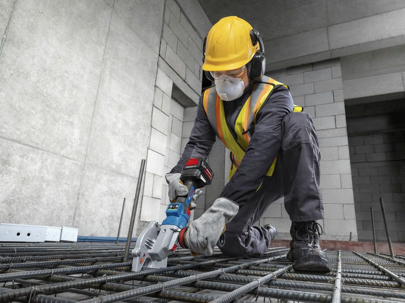 Một công nhân mặc đồ bảo hộ đang sử dụng máy cắt thép không dây để cắt các thanh thép.