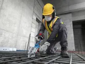 Một công nhân mặc đồ bảo hộ đang sử dụng máy cắt thép không dây để cắt các thanh thép.