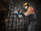 Một công nhân mặc đồ bảo hộ đang cắt thép cốt tại công trường bằng máy cắt thép cốt không dây.