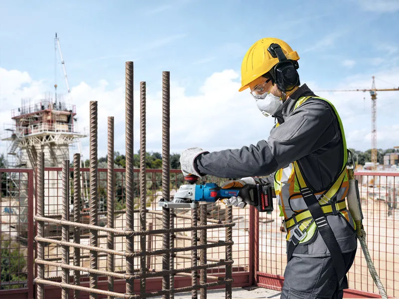 Một người đàn ông mặc đồ bảo hộ đang dùng dụng cụ không dây để cắt cốt thép tại công trường xây dựng.