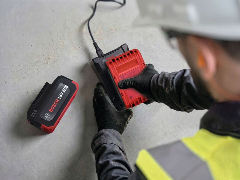 Một người mặc đồ bảo hộ đang lắp pin màu đỏ vào bộ sạc trên nền bê tông.
