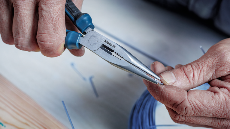 Một người dùng kìm mũi dài để xoắn một sợi dây nhỏ.