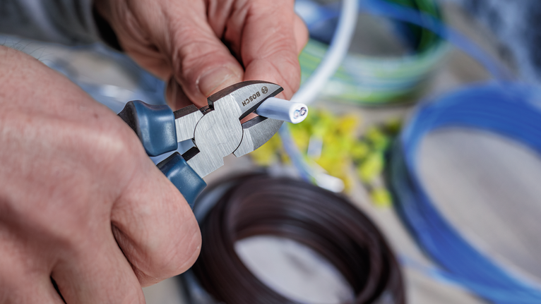 Một người đang dùng kìm cắt một sợi dây điện.