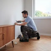 Một người đang mặc đồ bảo hộ và sử dụng tua vít không dây để cắm vào ổ cắm điện.
