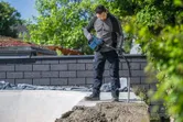 Một người đàn ông mặc đồ bảo hộ đang sử dụng dụng cụ điện để đầm nén bê tông ngoài trời.