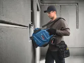 Một người mặc đồ bảo hộ đang kéo dây cáp điện vào hộp gắn trên tường.