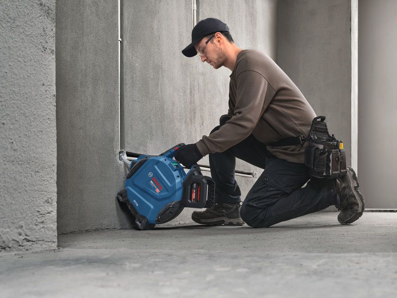 Một người đàn ông mặc đồ bảo hộ đang dùng dụng cụ điện để cắt một rãnh trên bê tông.